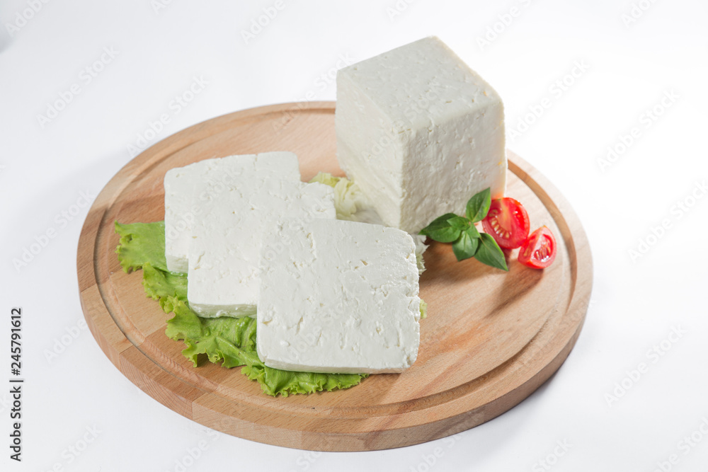 White cheese with some garnitures such as lettuce, cherry tomato slice and basil on a wooden plate, white background