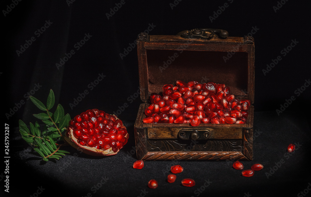 pomegranate on a dark background, pomegranate seeds in a wooden box, a piece of pomegranate next to a green leaf, rich in taste