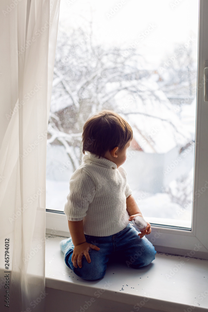 boy in a white sweater standing at the window on the windowsill boy in a white sweater standing at the window on the windowsill