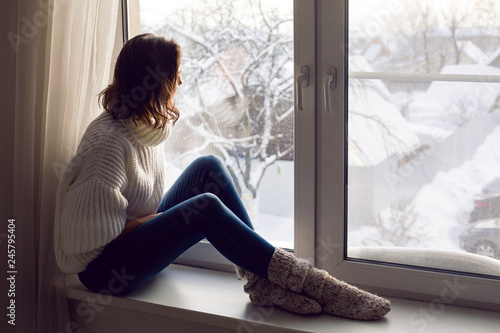 girl in a white knitted sweater sitting by the big window