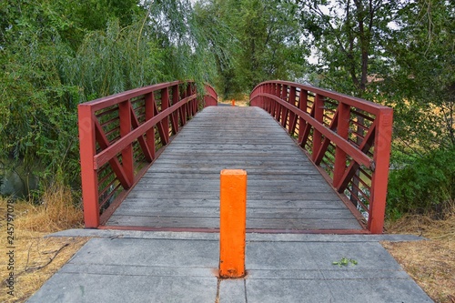 Views of Jordan River Trail Pedestrian and Train Track Bridge with surrounding trees, Russian Olive, cottonwood and muddy stream along the Wasatch Front Rocky Mountains, in Salt Lake City, Utah. photo