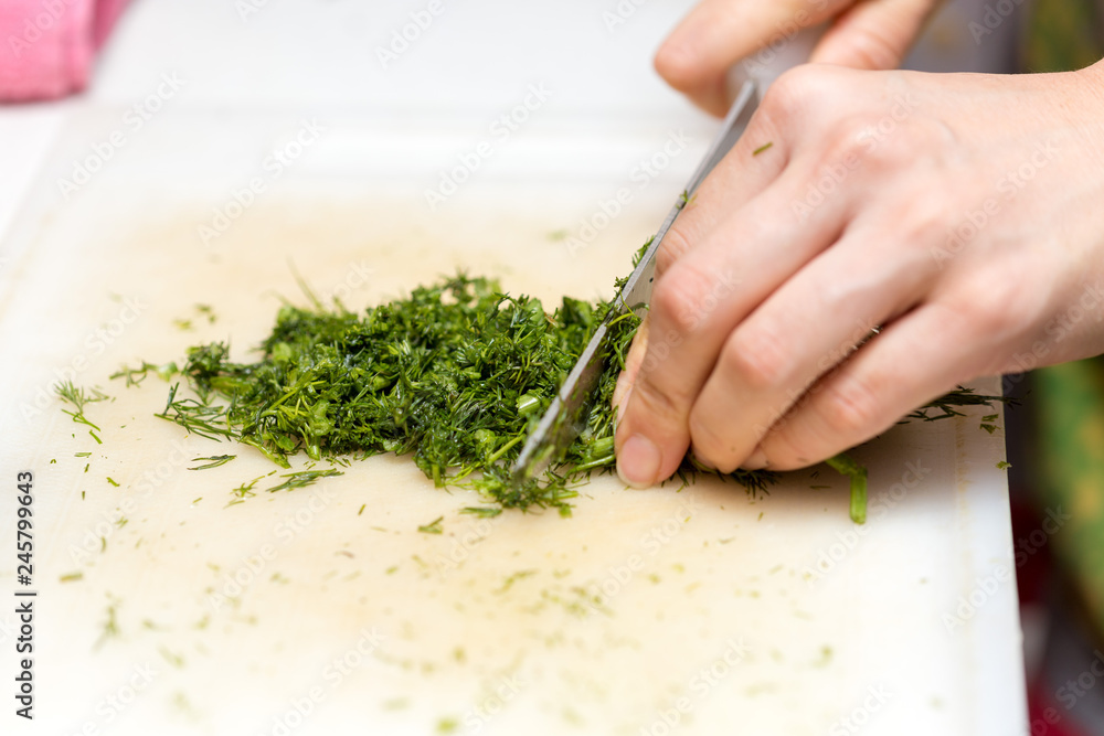 Female hands chopping the dill leaves on a cutting board with a knife. The concept of cooking Female hands chopping the dill leaves on a cutting board with a knife. The concept of cooking