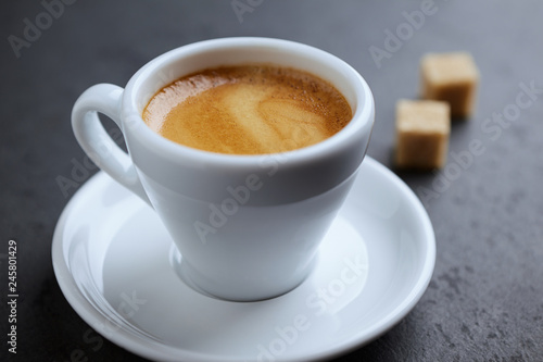 Cup of coffee and two brown sugar cubes on black stone background. Close up. 