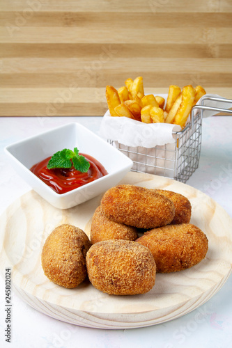 Ham and chicken croquettes on a wood plate with tomate and chips
