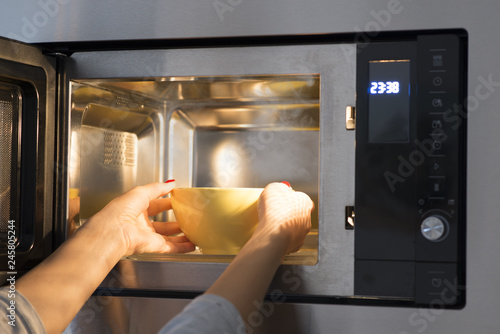 Cuadro en lienzo Woman at home heating food at microwave oven