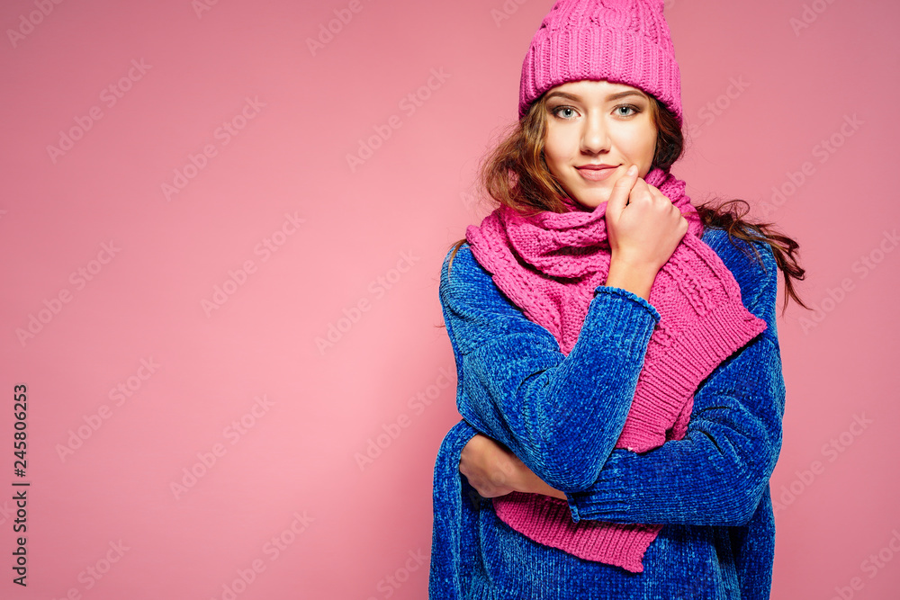 Modern young woman wearing blue sweater and pink hat, and scarf posing, making funny facial expression. Retouched, studio portrait. Modern young woman wearing blue sweater and pink hat, and scarf posing, making funny facial expression. Retouched, studio portrait.