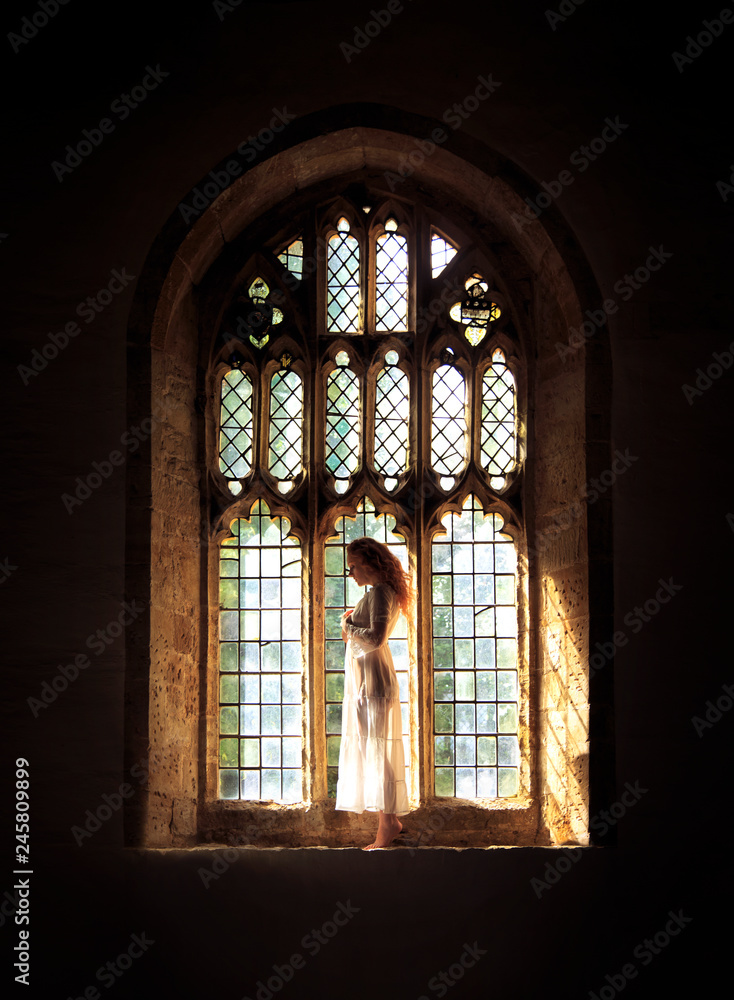 Beautiful woman posing in a Gothic church stained glass window