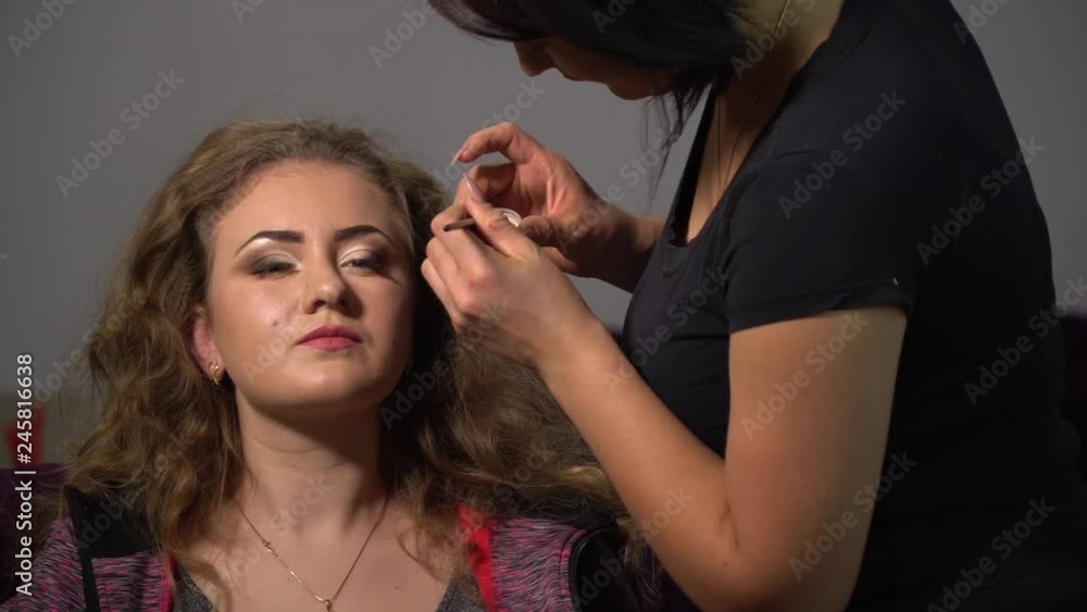 Beauty saloon. Young beautiful girl model is sitting in the chair. Makeup artist makes girl makeup. Makeup artist applies shadows on the eyelids of the model. Beauty saloon. Young beautiful girl model is sitting in the chair. Makeup artist makes girl makeup. Makeup artist applies shadows on the eyelids of the model.