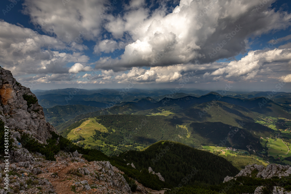 Scenic view with dark, blue, cloudy, sky from Rax plateau, Schneeberg massif, on valley with Puchberg village, rubble fields and green forest, Raxalpe, Alps, Lower Austria