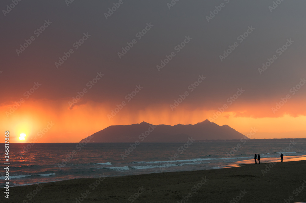 Obraz premium Rainy clouds with a red sunset sky in a seascape with Circeo in the background
