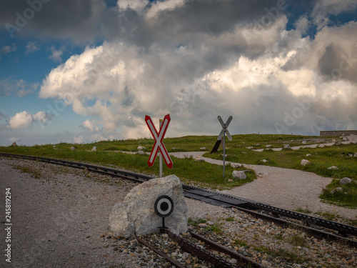 Cogwheel railway crossing with Saint Andrew's Cross near Hochschneeberg with cloudy sky in the scenic sunset, Raxalpe, Lower Austria photo