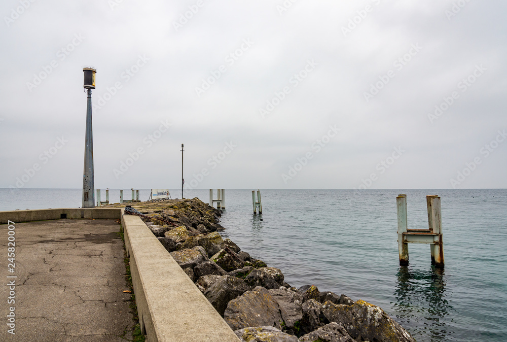 Outdoor scenery of riverside, embankment and pier at Geneva Lake without people with background of overcast cloudy sky in Lausanne, Switzerland.