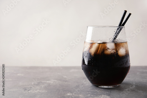 Glass of refreshing cola with ice on grey table. Space for text