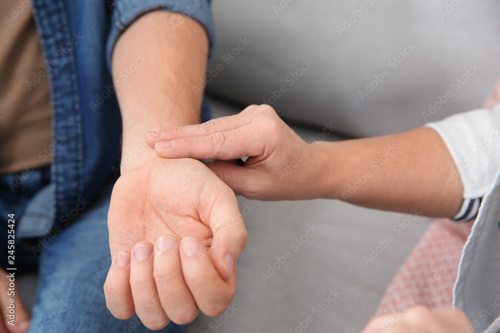 Mature woman checking man's pulse with fingers indoors, closeup Mature woman checking man's pulse with fingers indoors, closeup