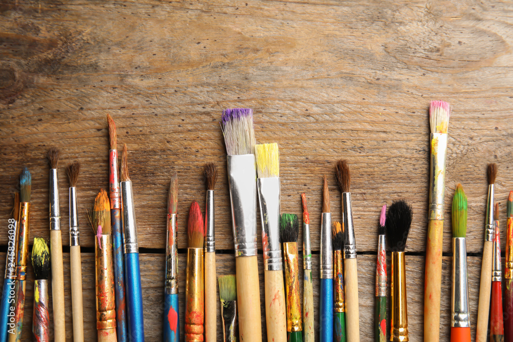 Fototapeta premium Different paint brushes on wooden background, top view with space for text