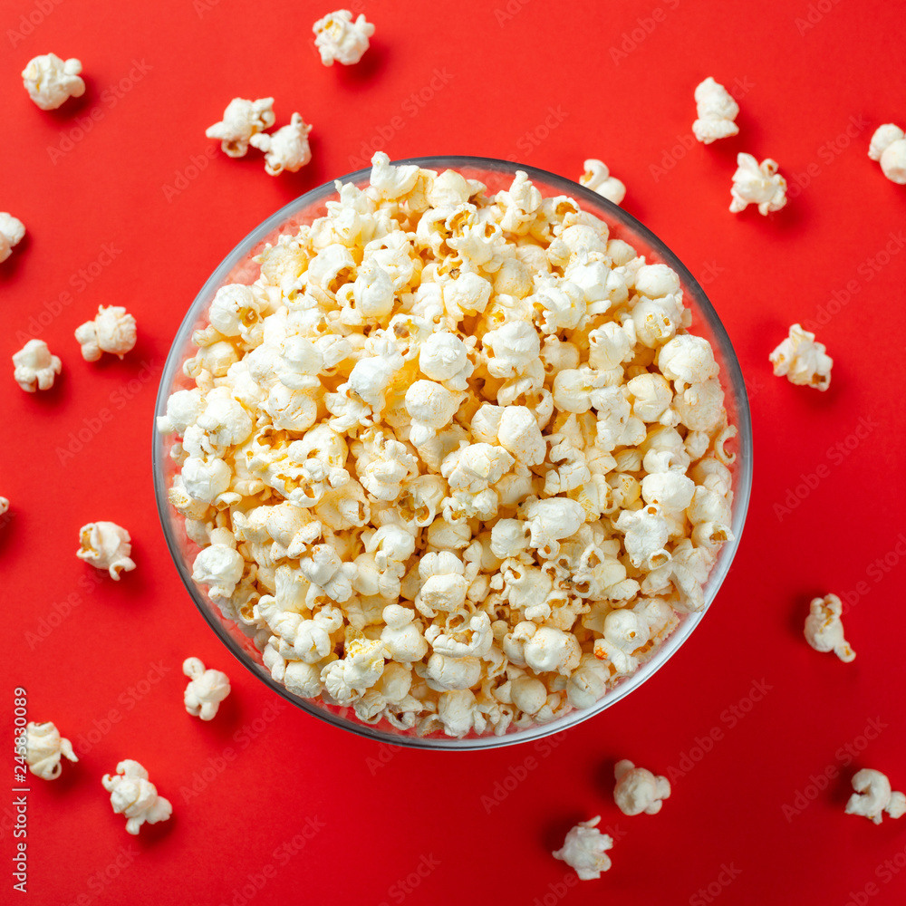 Glass bowl of salty popcorn on a red background. Top view with copy space. Flat lay Glass bowl of salty popcorn on a red background. Top view with copy space. Flat lay
