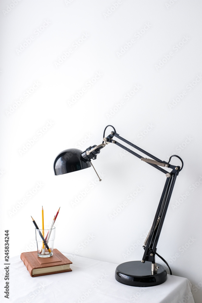 Retro black desk lamp a glass of sharp pencil a brown vintage notebook on white table top on white wall background with copy space product mock up placement Retro black desk lamp a glass of sharp pencil a brown vintage notebook on white table top on white wall background with copy space product mock up placement
