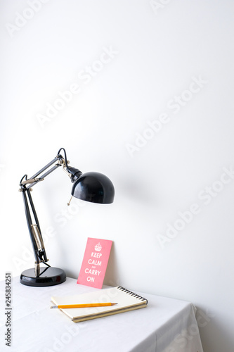 Retro black desk lamp white blank notepad and a yellow pencil and a motivational quote poster on white table top on white wall background with copy space product mock up placement