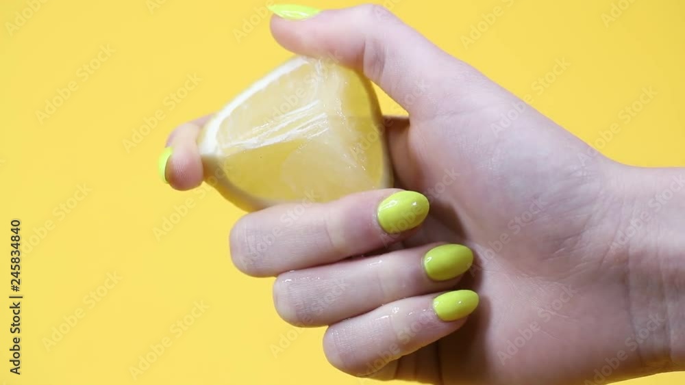 Hand with yellow fingernails squeezes fresh lemon as juice squirts out