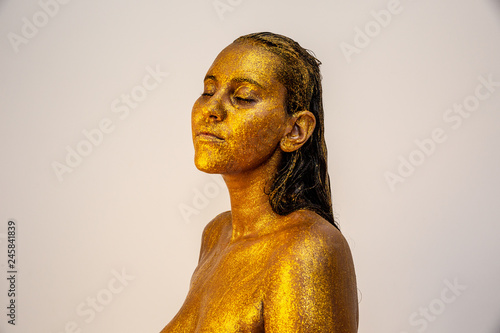Golden Fashion art Golden skin Woman face portrait closeup. Model girl with carnival holiday golden Glamour shiny professional makeup. Gold jewellery, jewelry, mask, carnaval. Gold metallic body.