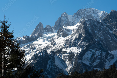 Jade dragon snow mountain situated in Yulong, Yunnan China. The snow covered mountain with rocky peaks with trees in the foreground giving a dramatic view.