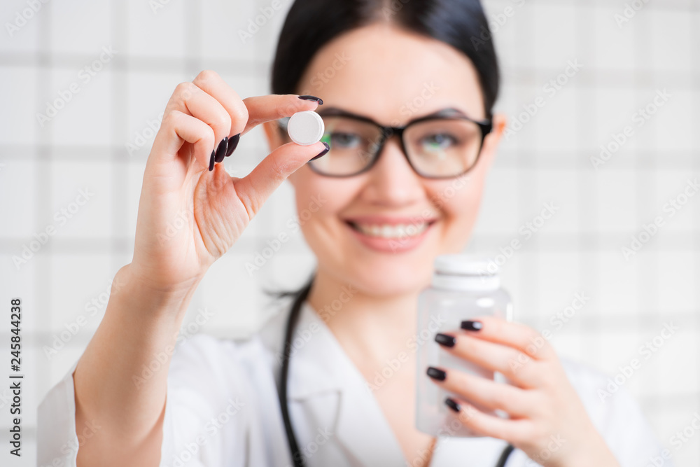 Young woman doctor holding and showing one white natural pill Young woman doctor holding and showing one white natural pill