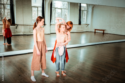 Red-haired slim dance teacher showing arm position to her student