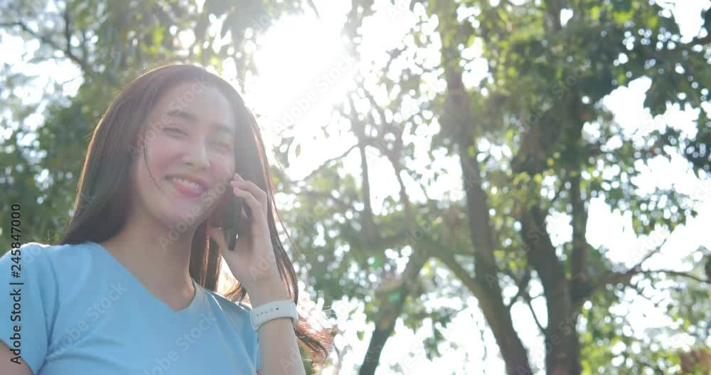 Beautiful young Asian woman using smartphone at park. Woman using smartphone with tree an natural in the background. Beautiful young Asian woman using smartphone at park. Woman using smartphone with tree an natural in the background.