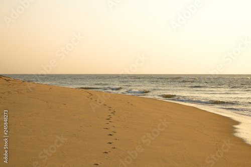 footprints on the yellow sand against the background of the ocean under a clear gray sky