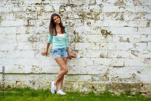 Young woman in short blue jeans shorts posing against a stone wall background