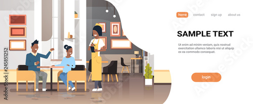 young waiter in uniform taking order from african american couple visitors sitting cafe table service concept modern restaurant interior horizontal flat copy space