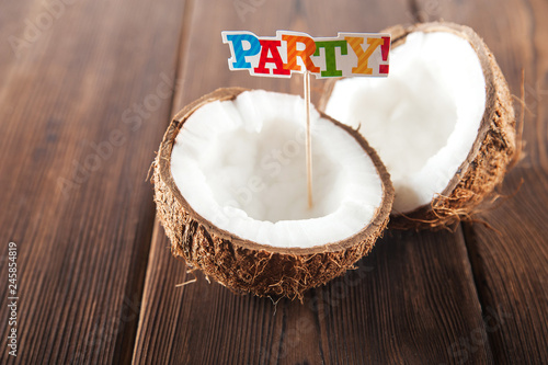 Coconut on the textural wooden background. Fragmented coconut close up. Topper inscription party 