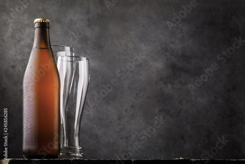 Bottle of light beer and two empty glasses on a wooden table as a human need. Food background