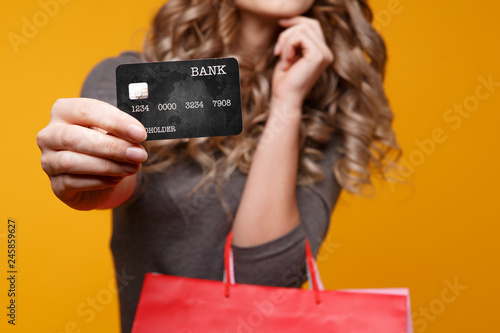 lose-up portrait of happy young brunette woman holding credit card and black shopping bags, looking at camera, isolated on yellow background photo