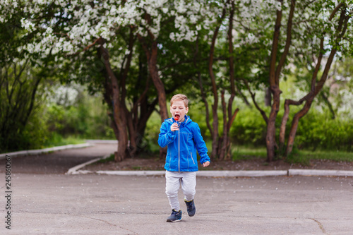 a stylish boy in a blue windbreaker and a Lollipop in his mouth runs along the path in the Park in the spring.