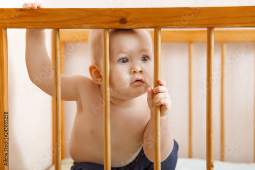 portrait of baby at home. Portrait of bored baby standing in crib. Baby stand alone in crib. Sad little baby. 