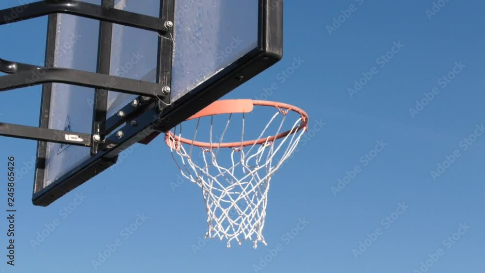 throw in a basketball hoop against a blue sky. Throwing ball into basketball ring against blue sky, through hoop, outdoors. Basketball hoop on the street against the blue sky. throw in a basketball hoop against a blue sky. Throwing ball into basketball ring against blue sky, through hoop, outdoors. Basketball hoop on the street against the blue sky.