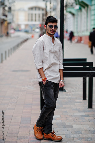 Stylish indian model man in casual clothes and sunglasses posed outdoor at street of India.