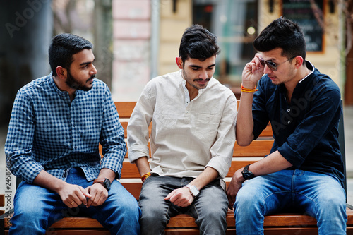 Group of three indian ethnicity friendship togetherness mans. Guys sitting on bench at street of India. photo