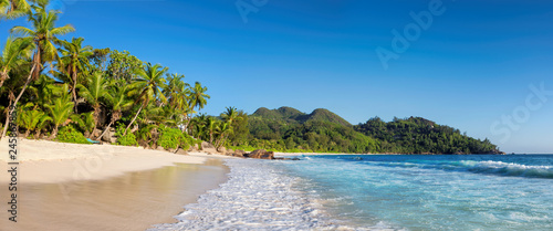 Panoramic view of sunset beach with palms and turquoise sea in Seychelles.