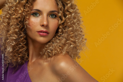 Smiling beautiful young woman. Girl with curly hair and braces. Yellow background. Concept for sale, copyspace.