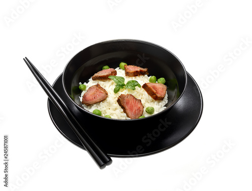 Rice with meat pieces, basil and green peas in a plate on a white background. 
