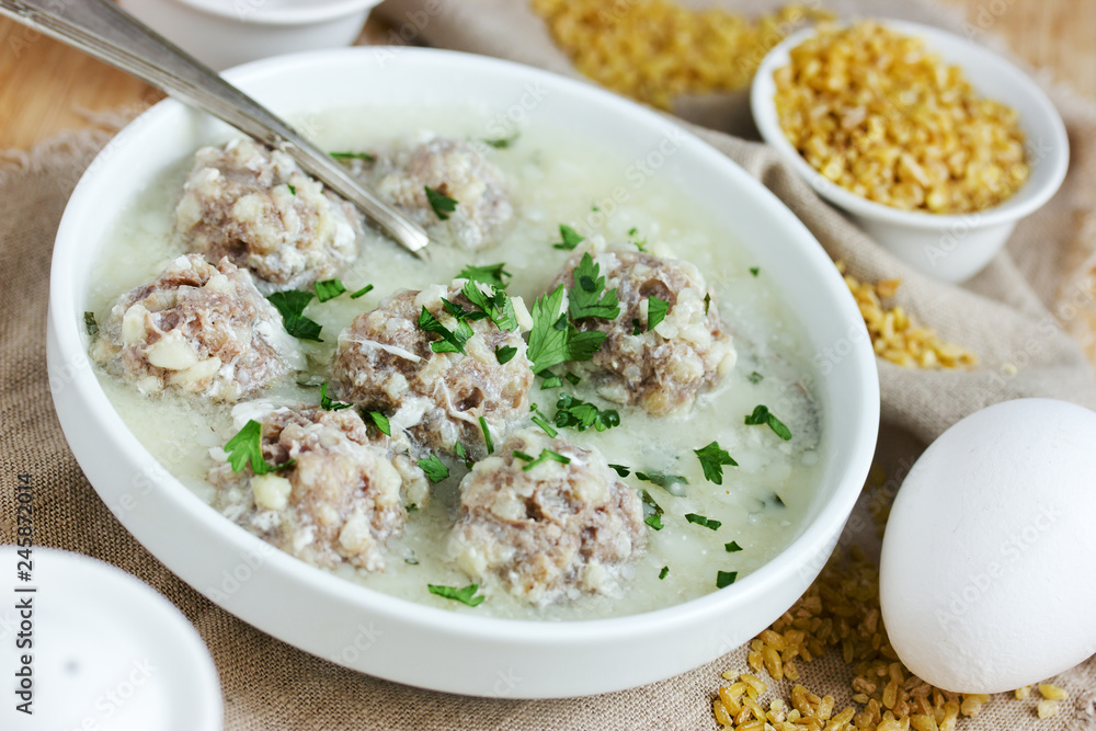 Armenian white sour soup on chicken broth with meatballs, bulgur and green parsley