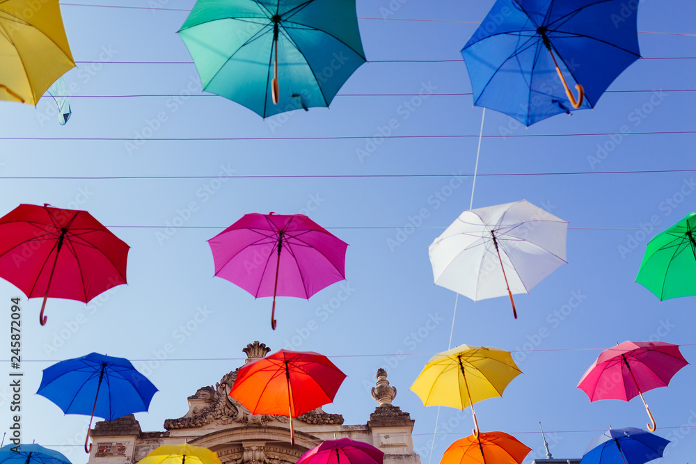 Lviv city colorful umbrellas on the street. Colored umbrellas hanging in the sky. Palace of arts. Street decorations. Multicolored umbrellas over blue sky. 