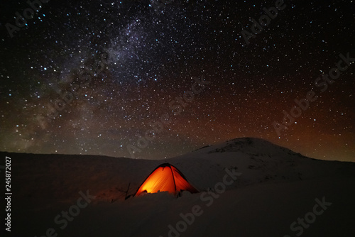 A charming night in the Carpathian Mountains with a tourist in a red tent and a Milky way with millions of stars in the sky.