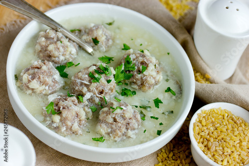 Armenian white sour soup on chicken broth with meatballs, bulgur and green parsley