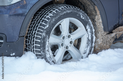 The wheel of a blue car stuck in the snow. The concept of a snowy winter, drifts on the road, adverse conditions, road accidents.