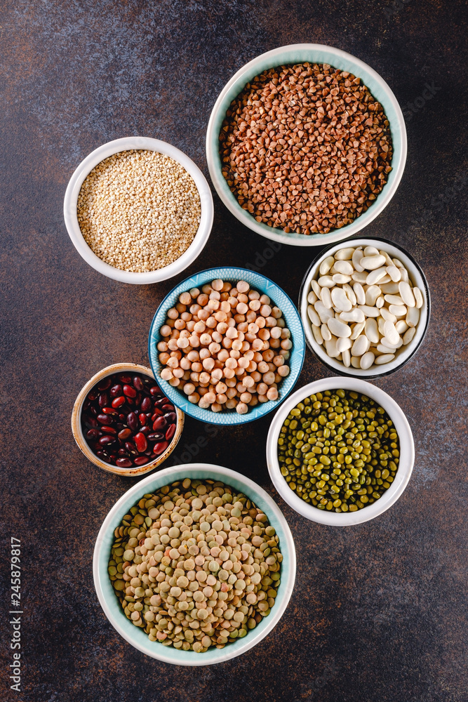 Top view on bowls with various grains on a textured dark background.