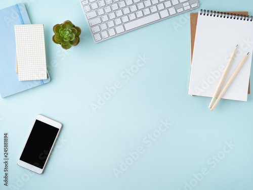 Top view of modern blue office desktop with blank notepad, computer, smartphone. Mock up, empty space photo