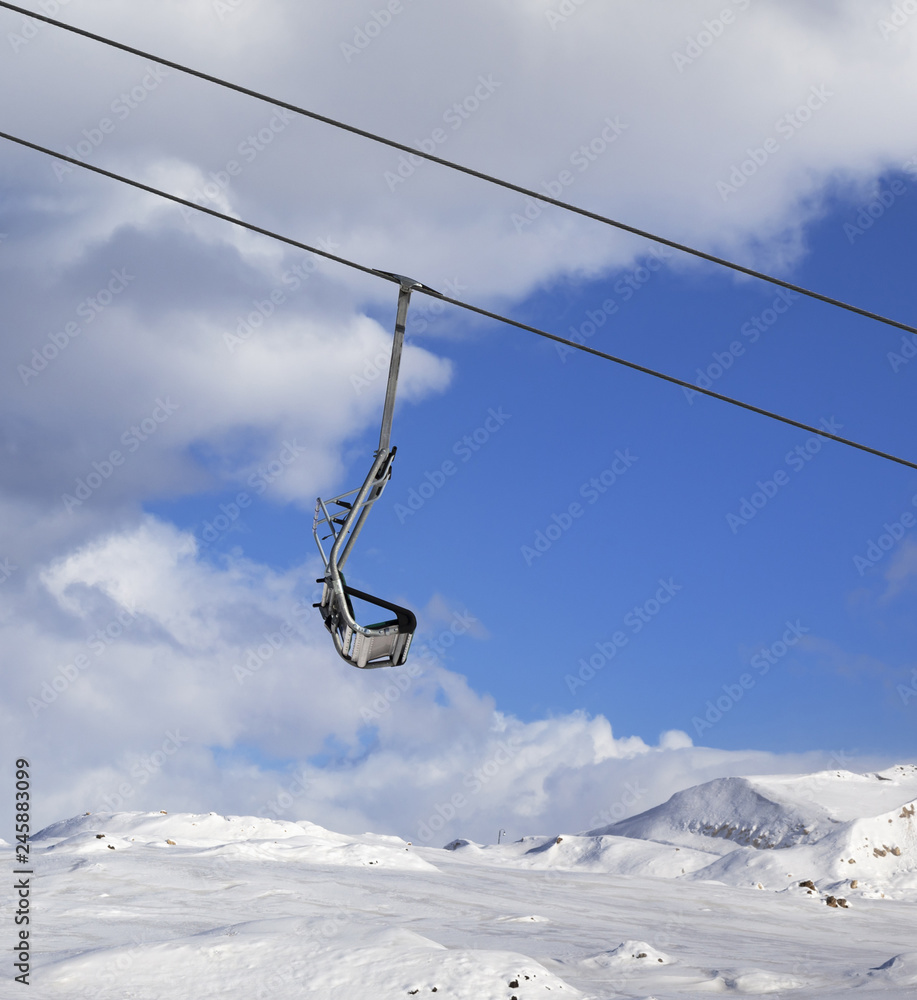 Snowy slope, chair-lift and blue sky with clouds at winter